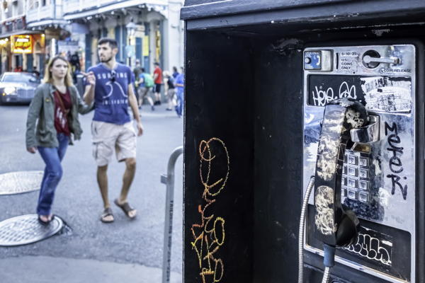 New Orleans, USA - Dec 4, 2017: Public phone booth that has been vandalized and covered with graffiti; along Bourbon Street in the French Quarter area. People in the background.